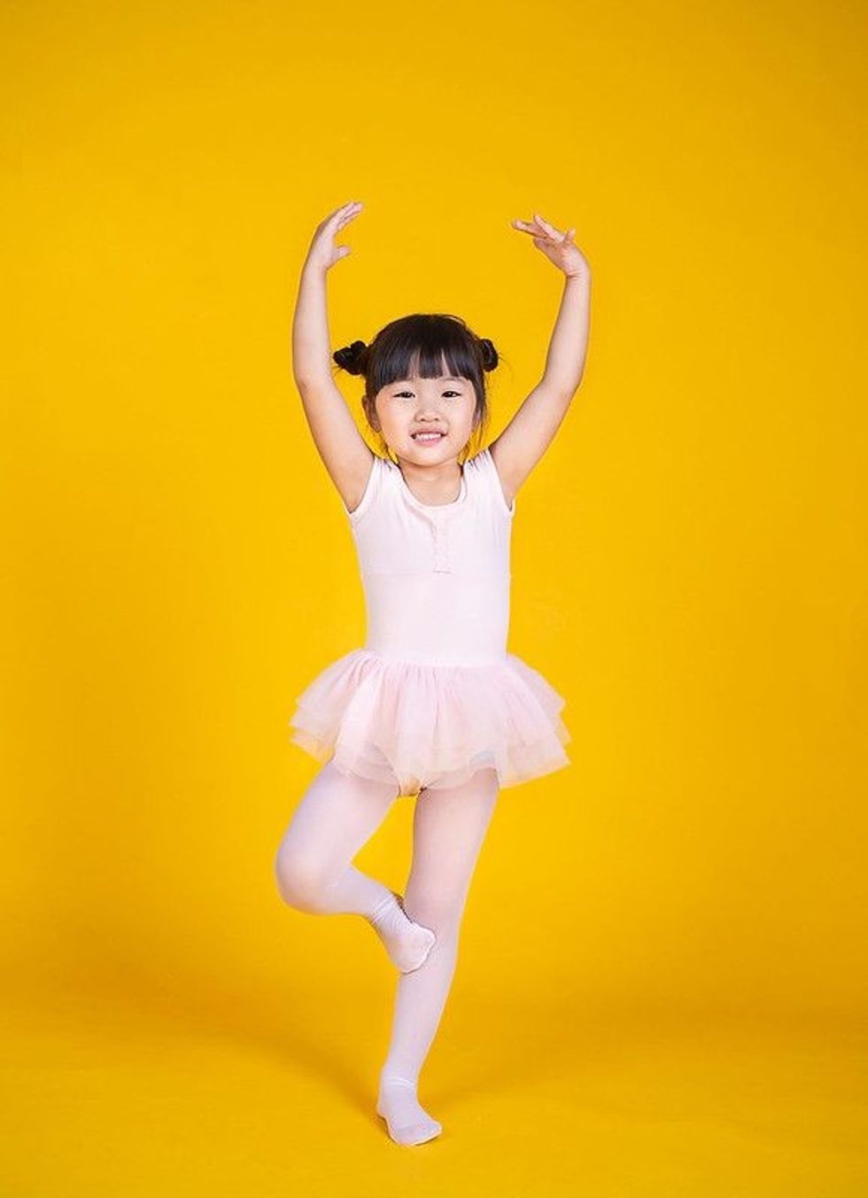Asian ethnic baby girl dressed as a ballet dancer on yellow background.