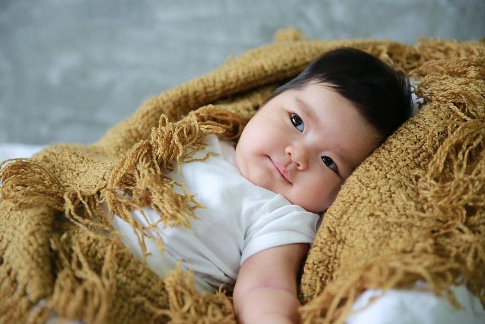 Asian ethnic baby lying on brown knitted blanket