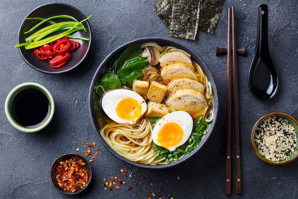 Asian noodle soup, ramen with chicken, tofu, vegetables and egg in black bowl.