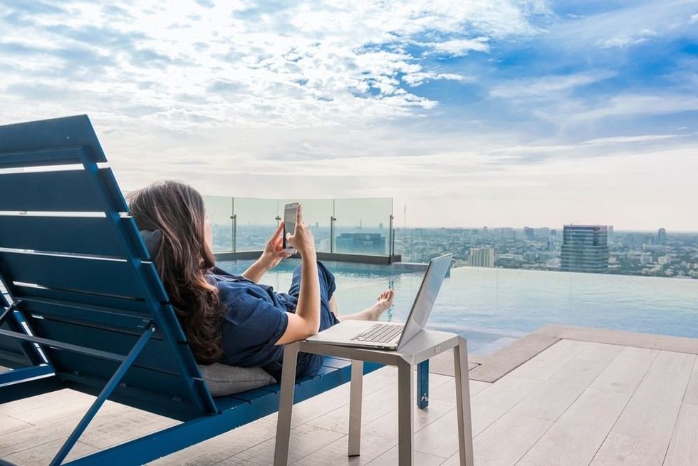 Asian woman using smartphone and working on a laptop with beautiful sky and clouds.