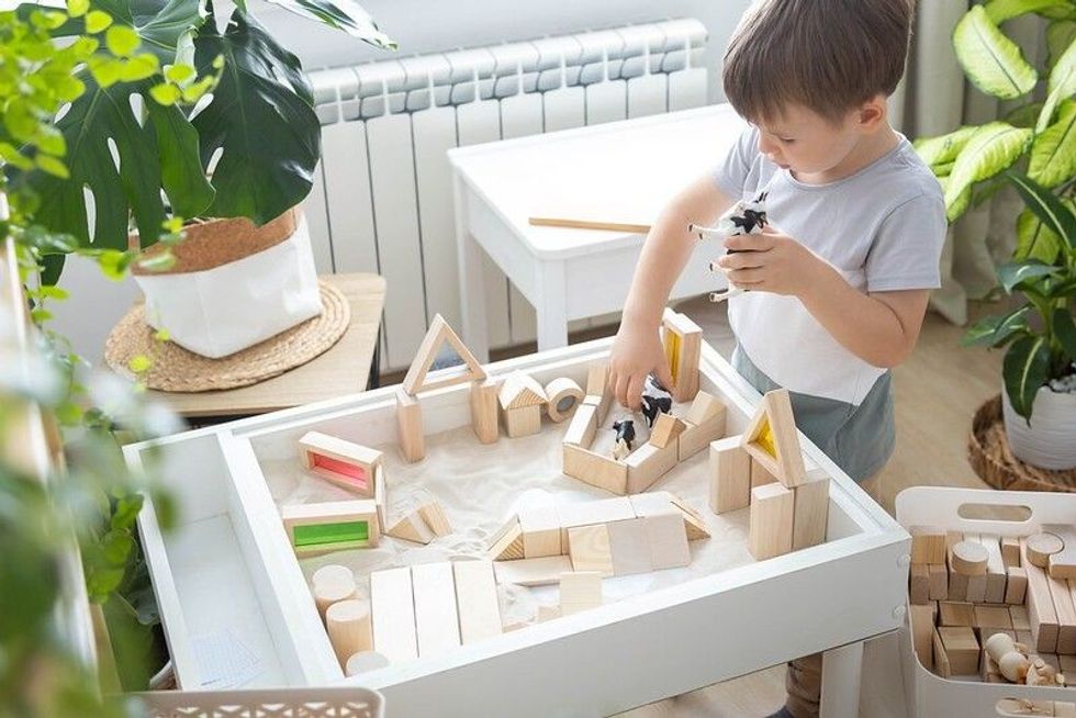 Baby Boy playing sensory box kinetic sand table with Montessori wooden materials and farm animals.