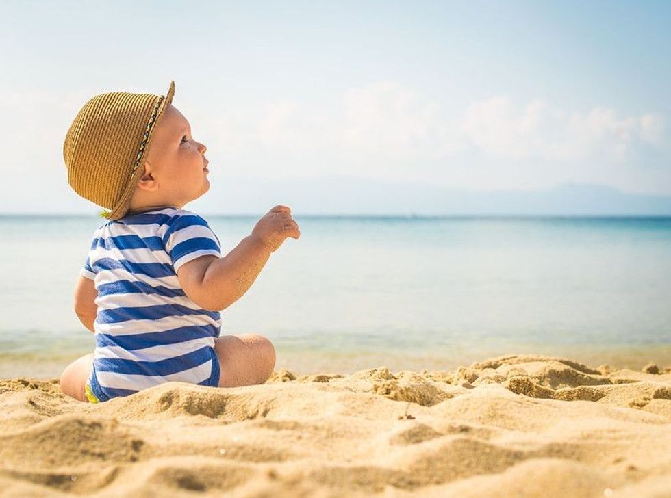 Baby boy sitting on beach in hat