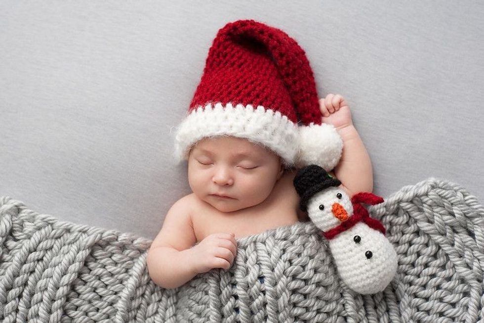 Baby boy wearing a crocheted Santa hat with snowman plush toy.