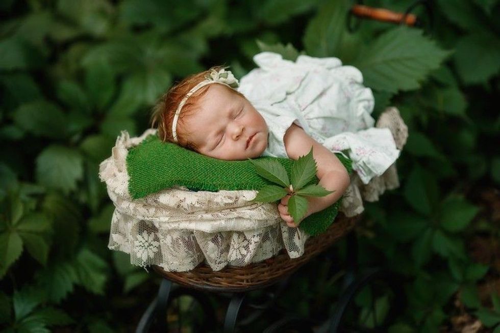 Baby girl sleeping in a basket holding a green leaf