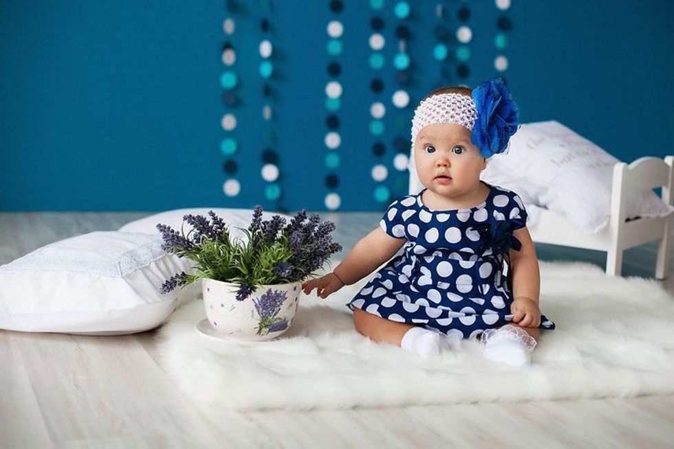 Baby girl wearing blue flower headband sitting next to lavender flowers