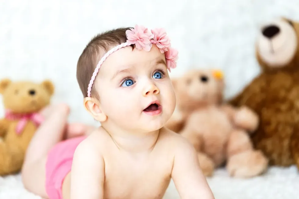 Baby girl with pink headband and blue eyes is smiling
