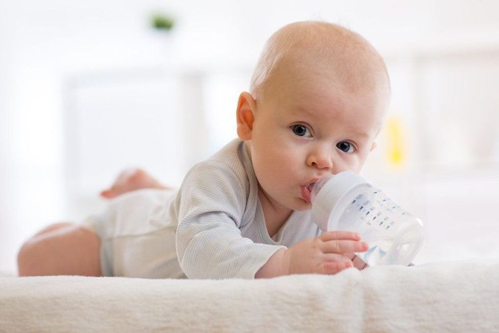 Baby lying on belly and drinking water from a bottle