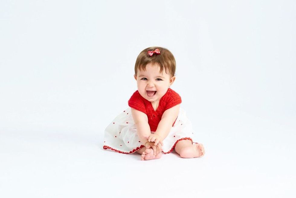 Baby sitting in red dress.