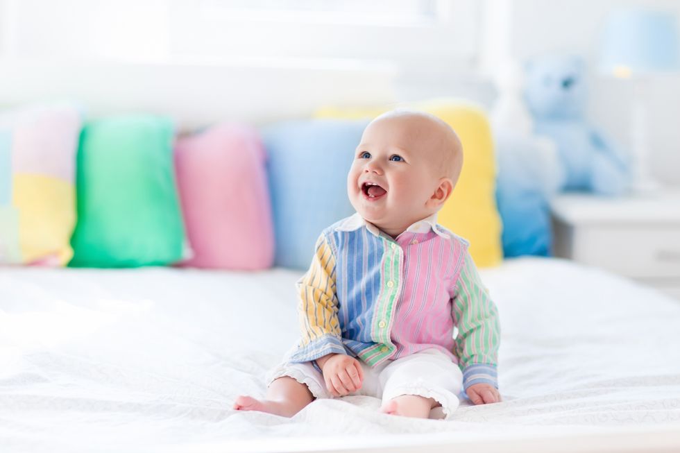 Baby sitting on on bed with colorful pillows on the background.