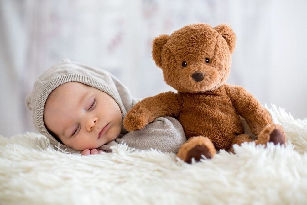 Baby sleeping in bed with teddy bear stuffed toy