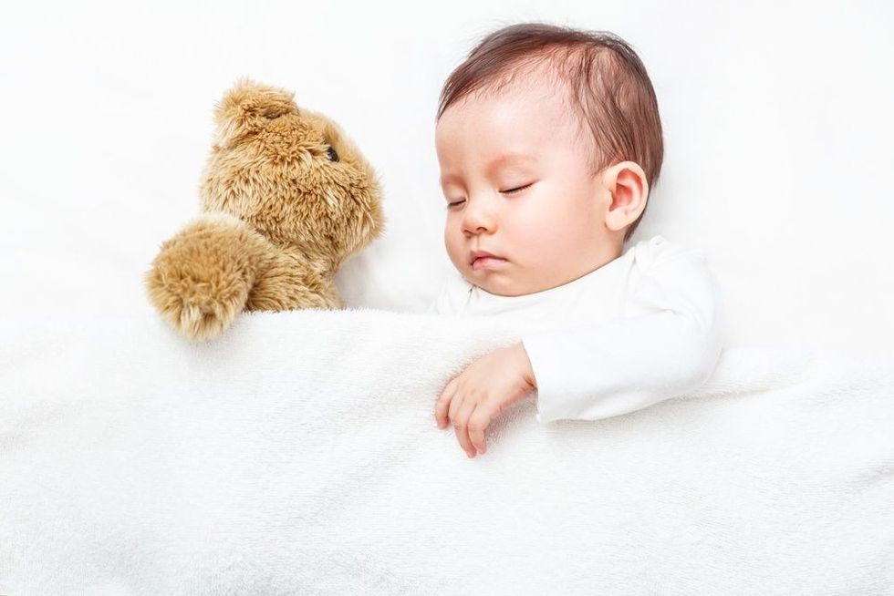 Baby sleeping with her teddy bear on the bed.