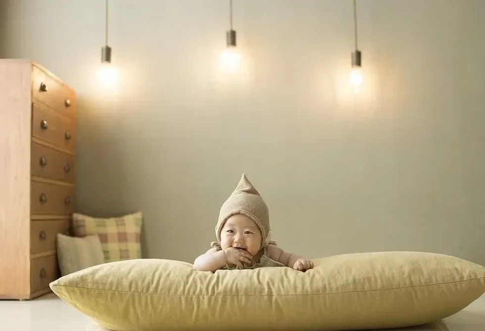 Baby wearing a hat lying on his tummy on a big cushion.