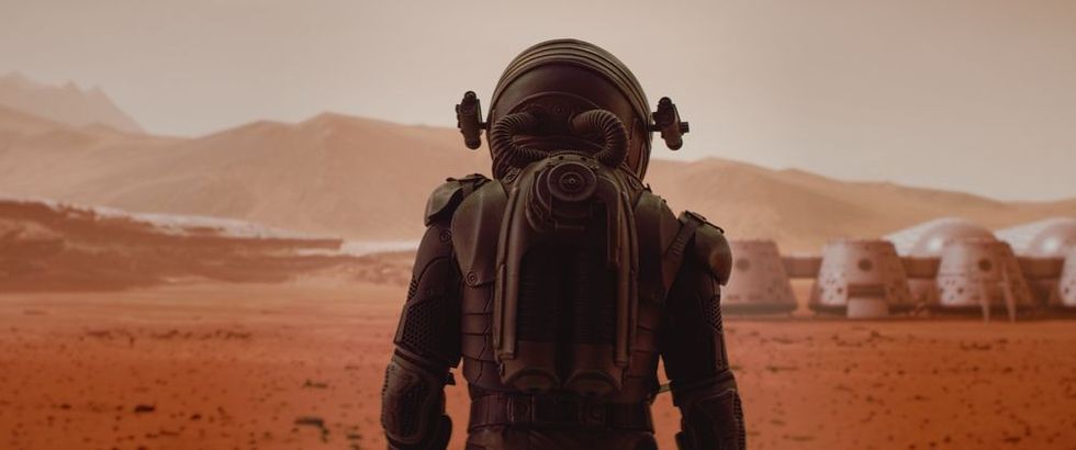 Back view of astronaut wearing space suit walking on a surface of a red planet.