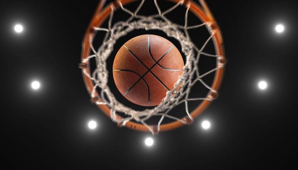 Basketball on hoop and lighting from roof stadium.