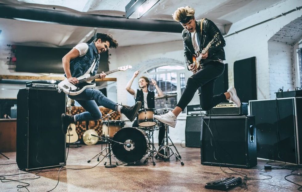 Bass guitar player, electric guitar player and drummer behind the drum set.