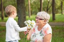 Beautiful boy giving a flower to grandma. Happy mothers day. Grandson and grandmother spending time together. Act of kindness to an elderly woman.