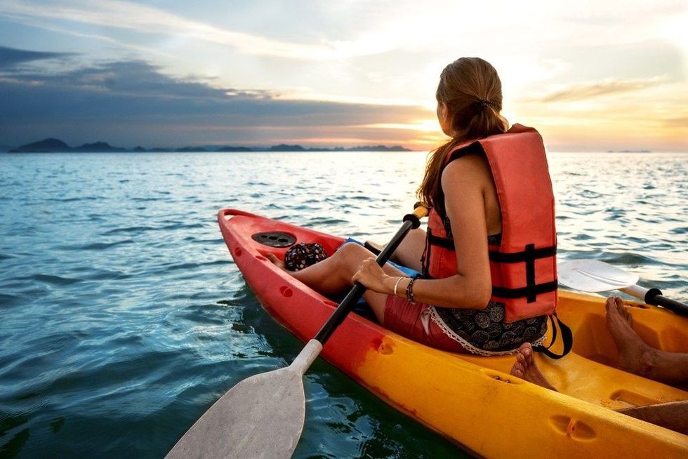 Beautiful young girl kayaking on lake together and smiling at sunset.