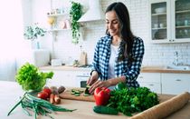 Beautiful young woman is preparing vegetable salad in the kitchen.