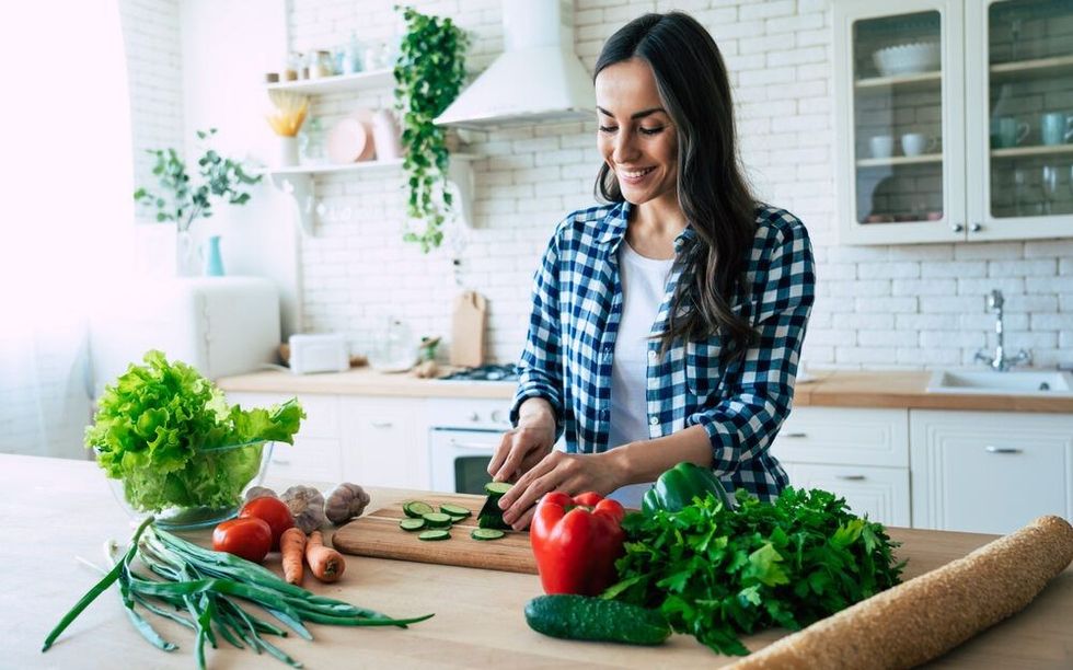 Beautiful young woman is preparing vegetable salad in the kitchen.