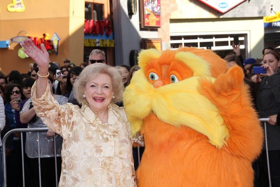 Betty White posing for the camera alongside the character lorax while waving for the camera