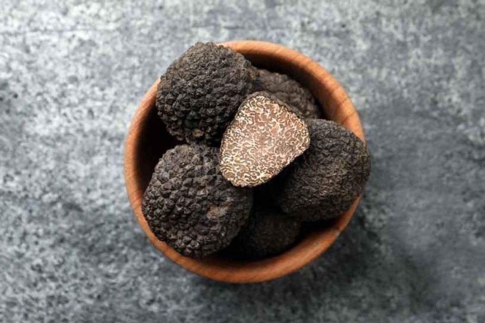 Black truffles in wooden bowl on grey table.