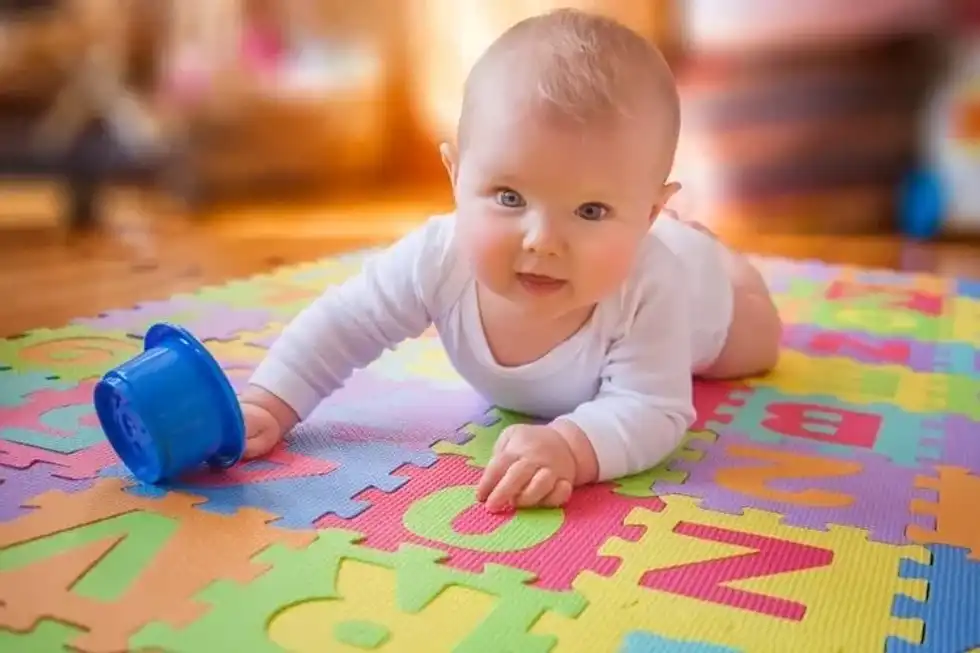 Blue-eyed reaching for cup on alphabet mat