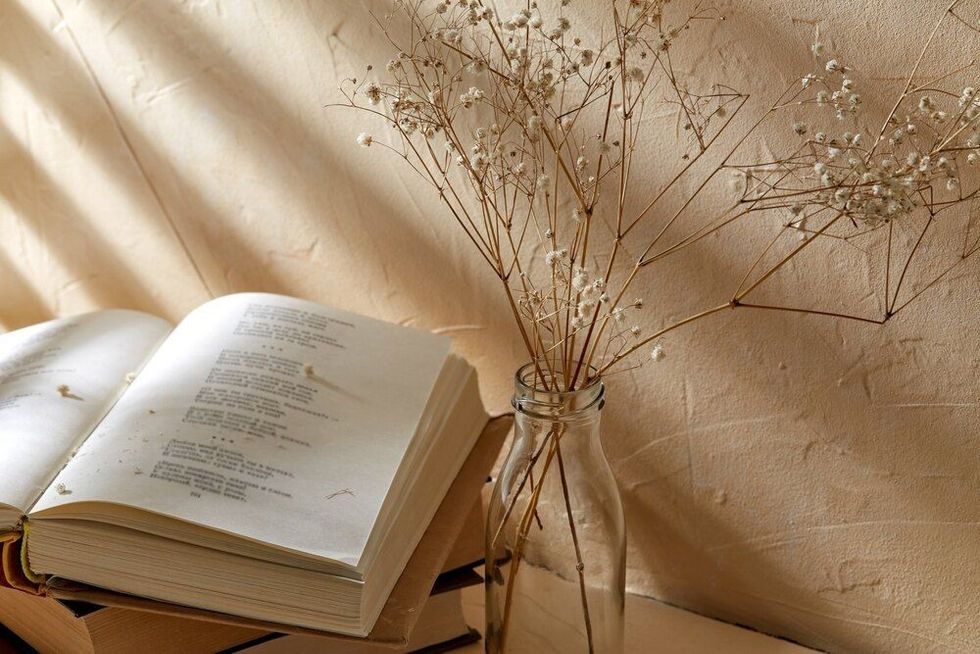 Books and decorative dried baby's breath flowers in glass bottle over beige background 