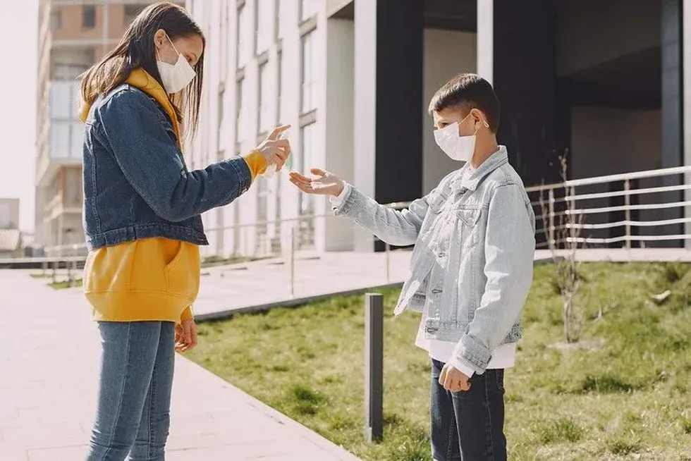 Boy and girl wearing masks spraying hand sanitiser