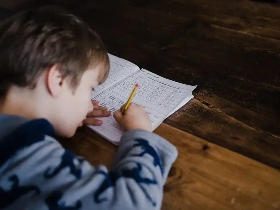 Boy sat at the table doing KS2 fractions in his workbook.