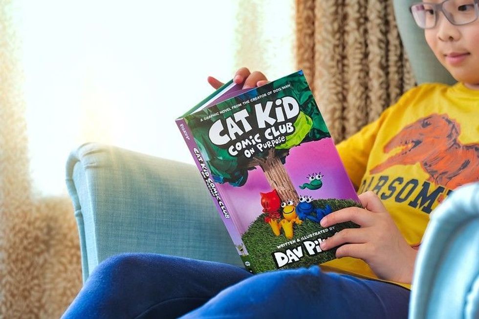 Boy student reading latest graphic novel comics book Cat Kid on sofa.