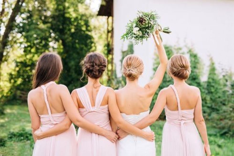 bride standing with her back in a white wedding dress and raised hand with three bridesmaids