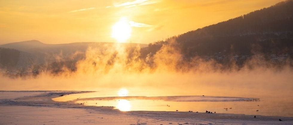 Bright orange winter sun shines through fog above river
