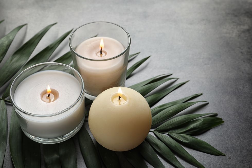 Burning wax candles and tropical leaf on table.
