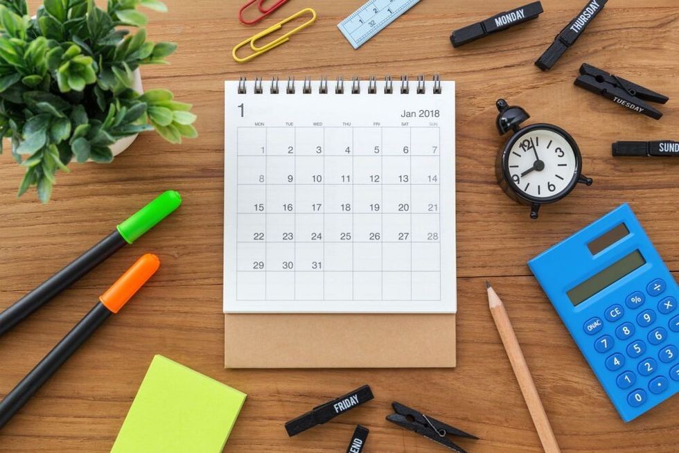 Calendar on wooden table with clock and calculator from top view.