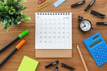Calendar on wooden table with clock and calculator from top view.