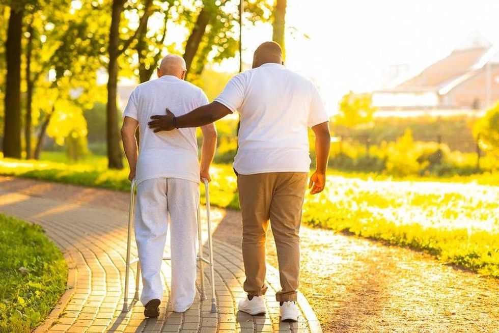 Caregiver taking precaution while an old man is walking with walker.