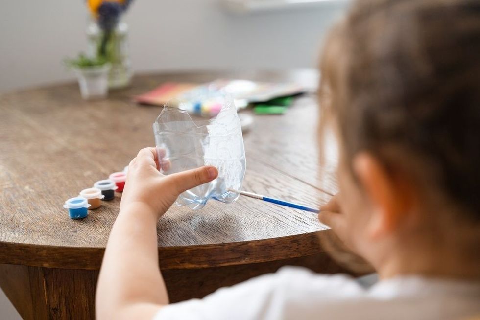 Caucasian preschool girl doing crafts with plastic bottle and paints.