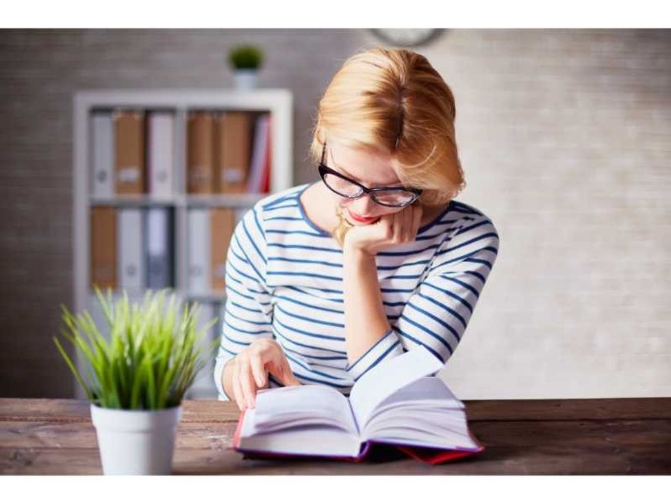 Charming girl sitting by wooden table and reading book