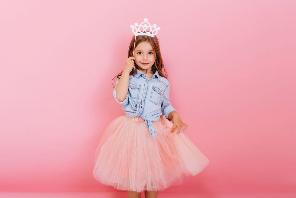 Cheerful little girl with long brunette hair holding princess crown