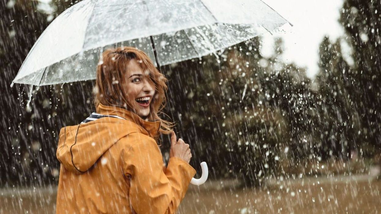 Cheerful pretty girl holding umbrella while raining outside.