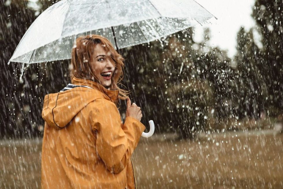 Cheerful pretty girl holding umbrella while strolling outside. She is turning back and looking at camera with true delight and sincere smile.