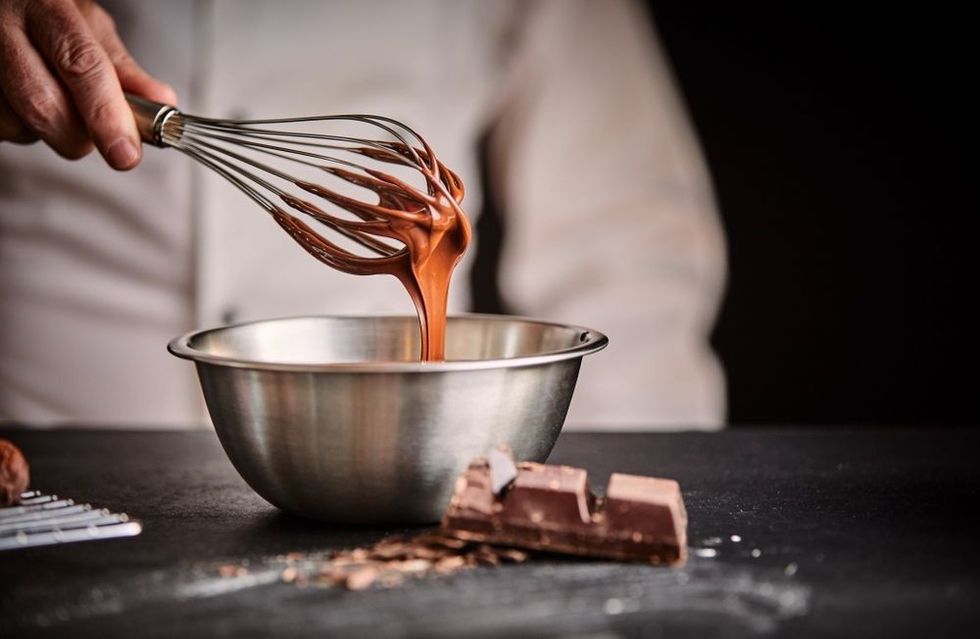 Chef whisking melted chocolate in a stainless steel mixing bowl