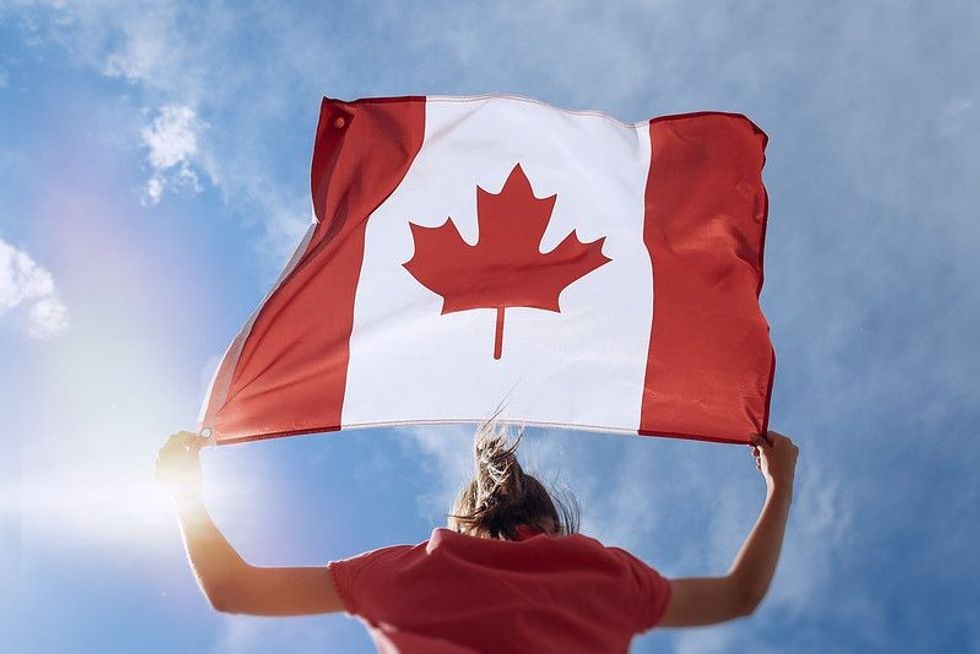 Child girl is waving Canadian flag on top of mountain at sky.