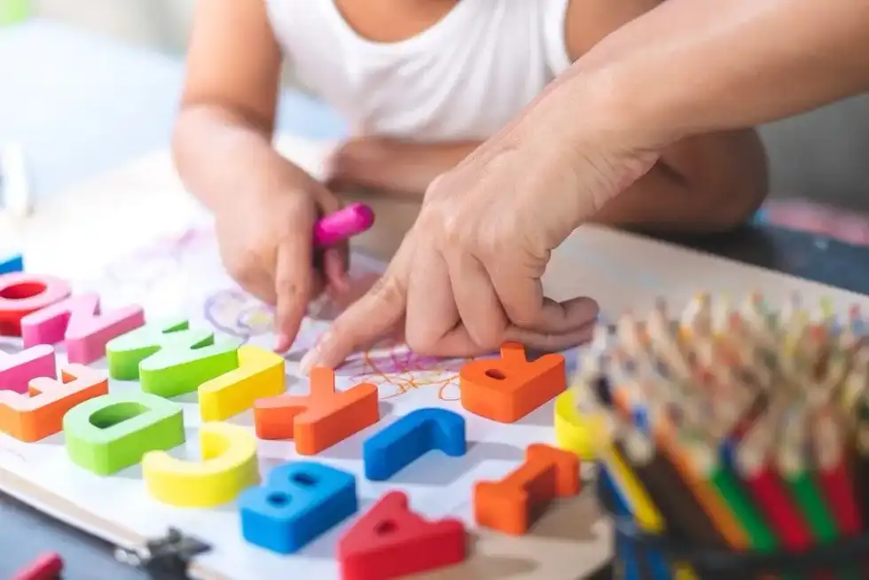 Child learning phonics and letters using colourful plastic letters laid out on the table.