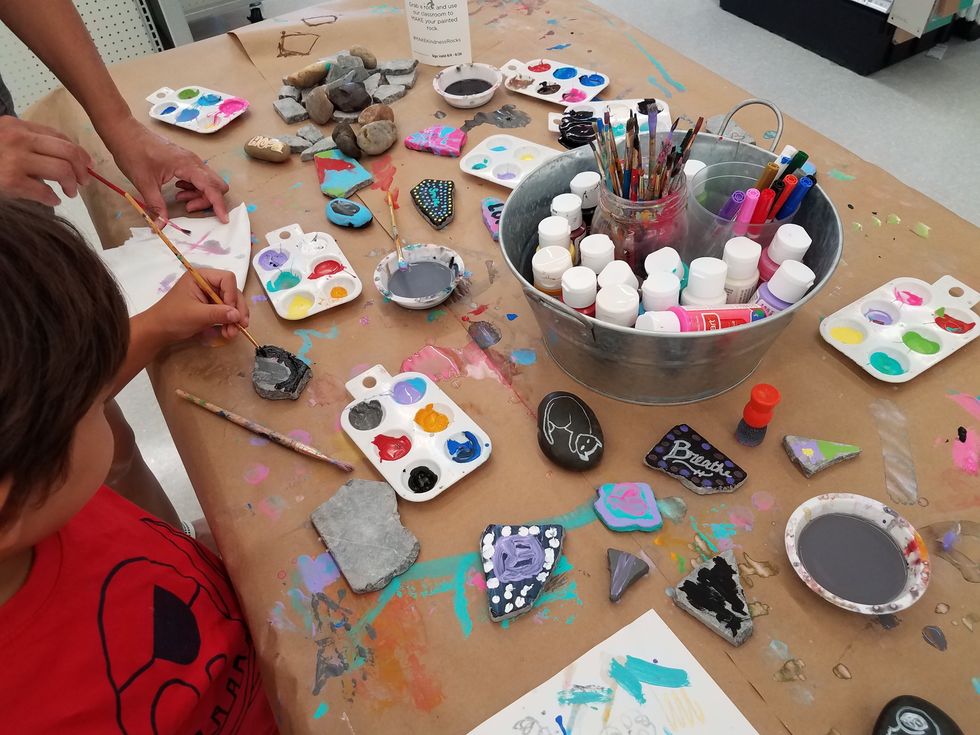 Child painting rocks on a table with colored paints.