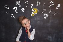 Child with thoughtful face and many questions drawn on chalkboard.