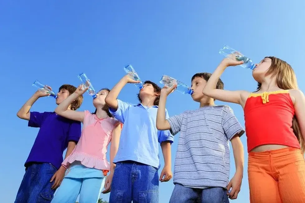 Children drinking water from bottles against the blue sky