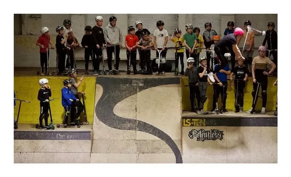 Children in protective gear waiting at the top of a ramp at LS-TEN Skatepark.