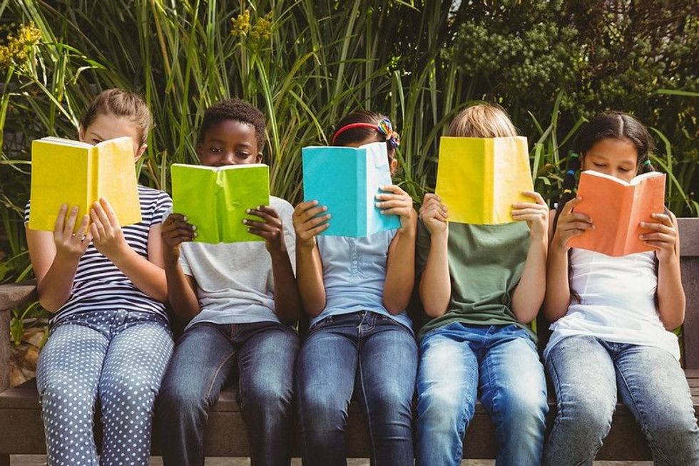 Children sitting in row and reading books at the park