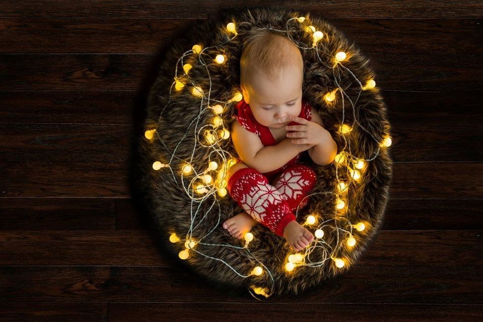 Christmas baby sleeping in fur nest with lights on dark wooden background holidays inspiration.